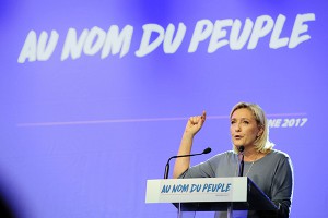 French far-right Front National (FN) party's President, Marine Le Pen, delivers a speech on stage during the FN's summer congress in Frejus, southern France, on September 18, 2016. Marine Le Pen's slogan reading "In the name of the [French] people" is seen on the rostrum. / AFP PHOTO / Franck PENNANT